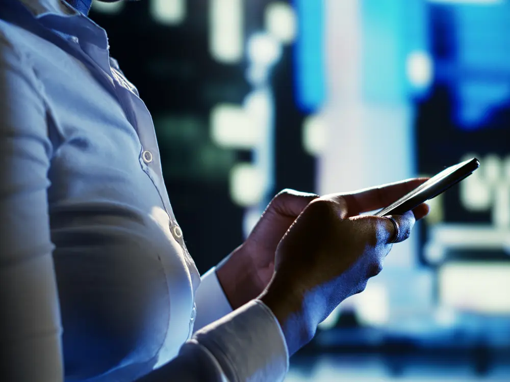 A passenger checking a rideshare app on a phone on a city street at night.